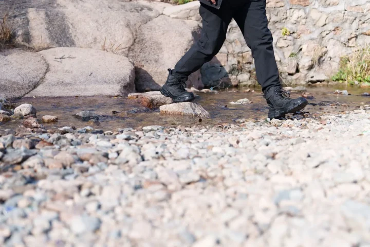Hiker in boots crossing a shallow rocky stream