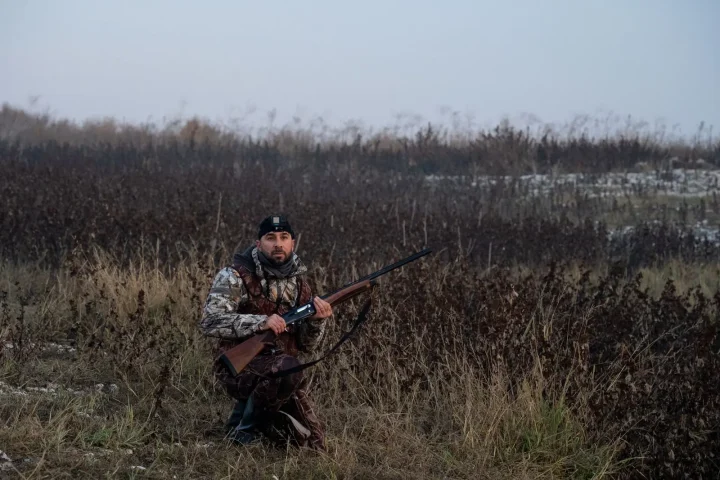 Hunter in camouflage kneeling in dry marsh grass