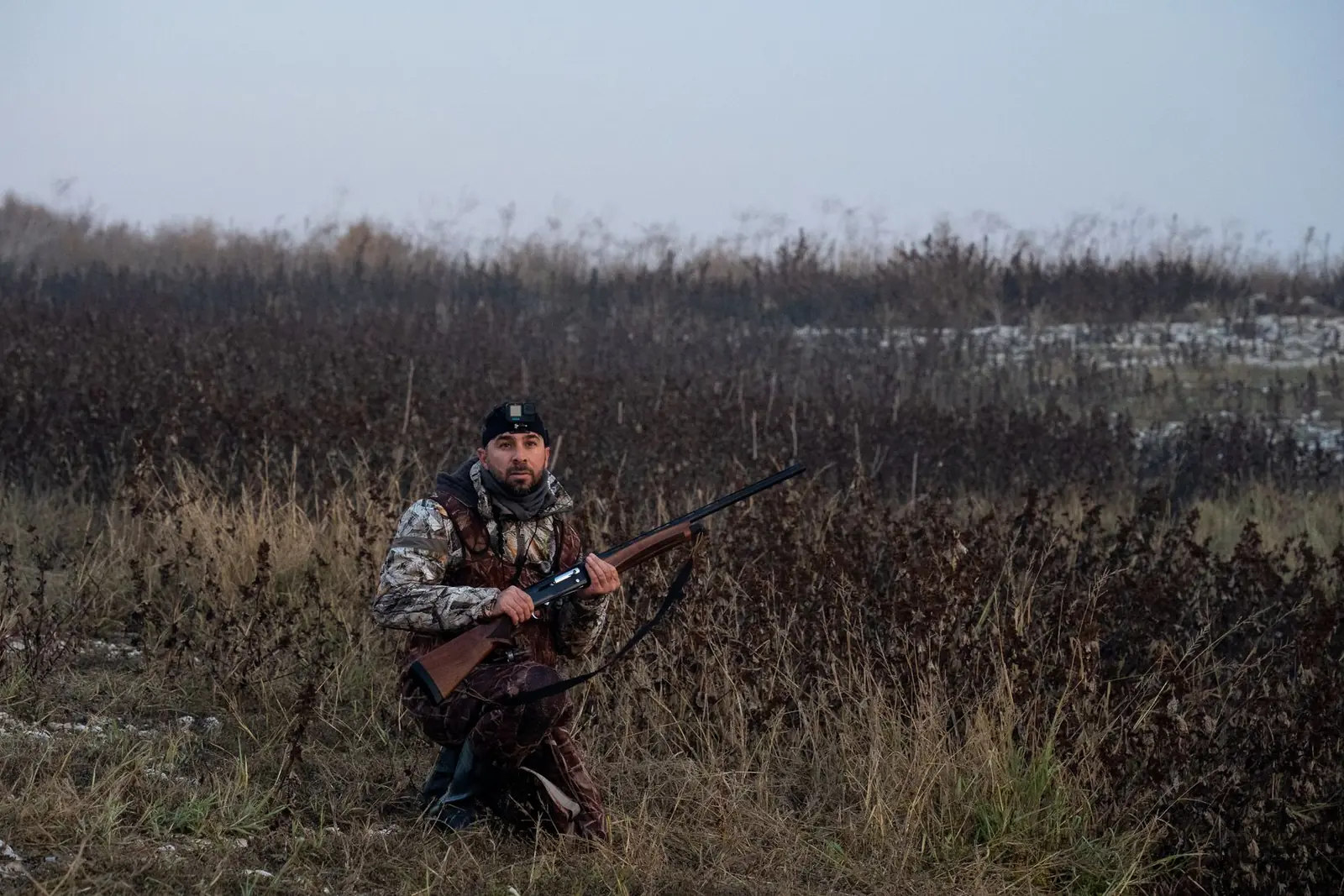 Hunter in camouflage kneeling in dry marsh grass
