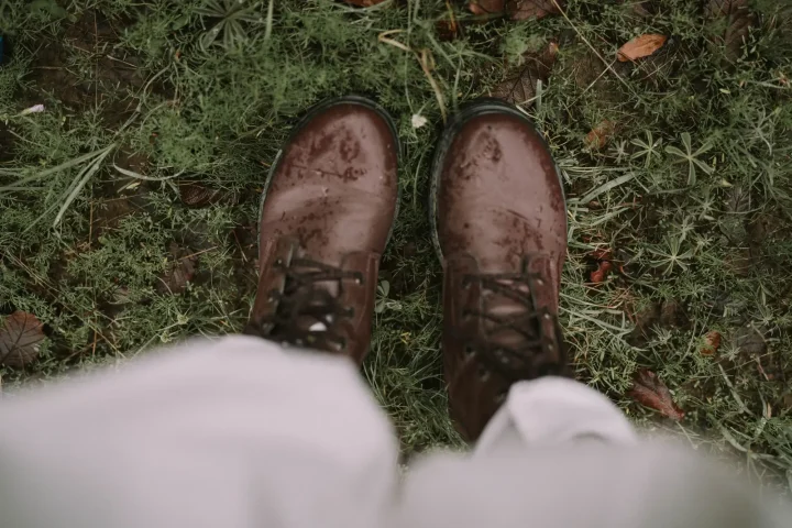 Muddy brown leather boots on wet grass seen from above
